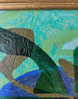 Close up of a framed, green & blue mixed media artwork with abstract design.