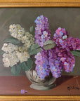 Close up of a framed, vintage artwork of purple and white flowers on a dark background.