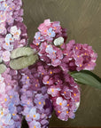 Close up of a framed, vintage artwork of purple and white flowers on a dark background.
