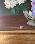 Close up of a framed, vintage artwork of purple and white flowers on a dark background.