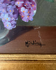 Close up of a framed, vintage artwork of purple and white flowers on a dark background.