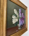 Close up of a framed, vintage artwork of purple and white flowers on a dark background.