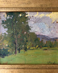 Close up of a framed vintage oil painting of a landscape with trees and a meadow.