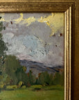 Close up of a framed vintage oil painting of a landscape with trees and a meadow.