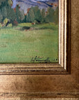 Close up of a framed vintage oil painting of a landscape with trees and a meadow.