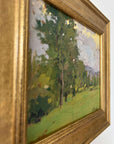 Close up of a framed vintage oil painting of a landscape with trees and a meadow.