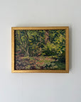 A framed vintage landscape oil painting depicting a lush green forest with trees and sunlight, enclosed in a gold frame. Available at Hue.