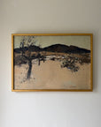 A framed vintage landscape painting. The artwork depicts a dry, sandy scene with a dark tree in the foreground, sparse shrubs, and dark hills under a pale sky. Available at Hue.