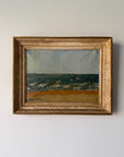 A framed vintage oil painting of a coastal landscape with a sandy beach, blue-green sea, and a small boat under a pale sky, housed in an ornate gold frame. Available at Hue.