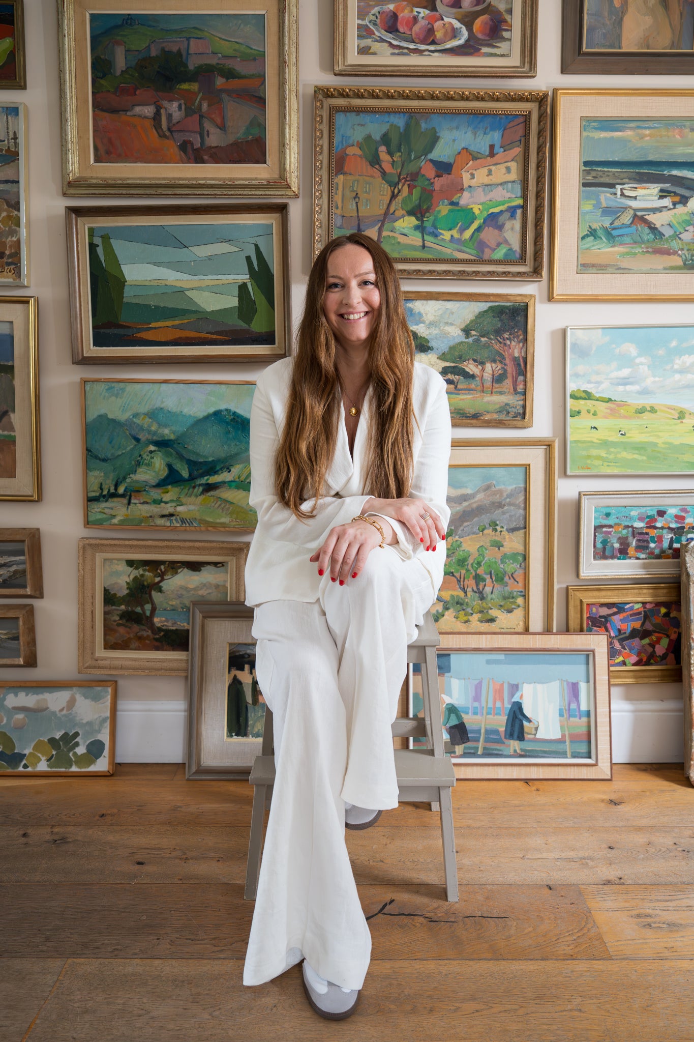 Woman in a white outfit sitting in front of a wall of framed paintings