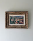 A framed vintage landscape oil painting of a hillside village with green trees and terracotta roofs. Available at Hue.