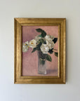 A framed vintage oil painting on canvas of a bouquet of white roses in a glass vase on a dusty pink background. Available at Hue.