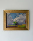 A framed vintage landscape oil painting featuring a green tree under a dramatic blue and white sky. Available at Hue.