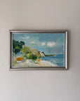 A framed vinatge landscape oil painting depicting a coastal scene with blue water, green trees, and a sandy shore. Available at Hue.