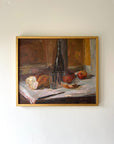 A framed vintage oil painting of a still life supper scene with bread and wine. Available at Hue.