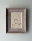 A small vintage framed ink sketch featuring a nude seated figure on a cream background, housed in a rustic, textured gray-brown frame. Available at Hue.