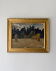 A framed vintage landscape painting. The painting depicts a field with hayricks under a dark forest and cloudy sky, enclosed in a wide gold frame. Available at Hue.
