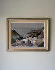 A framed vintage coastal landscape paintingl. The artwork depicts rocky cliffs, a shoreline, and muted water in soft gray, brown, white, and green tones. Available at Hue.