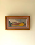 A framed vintage landscape oil painting of houses with red roofs and a yellow building. Available at Hue.