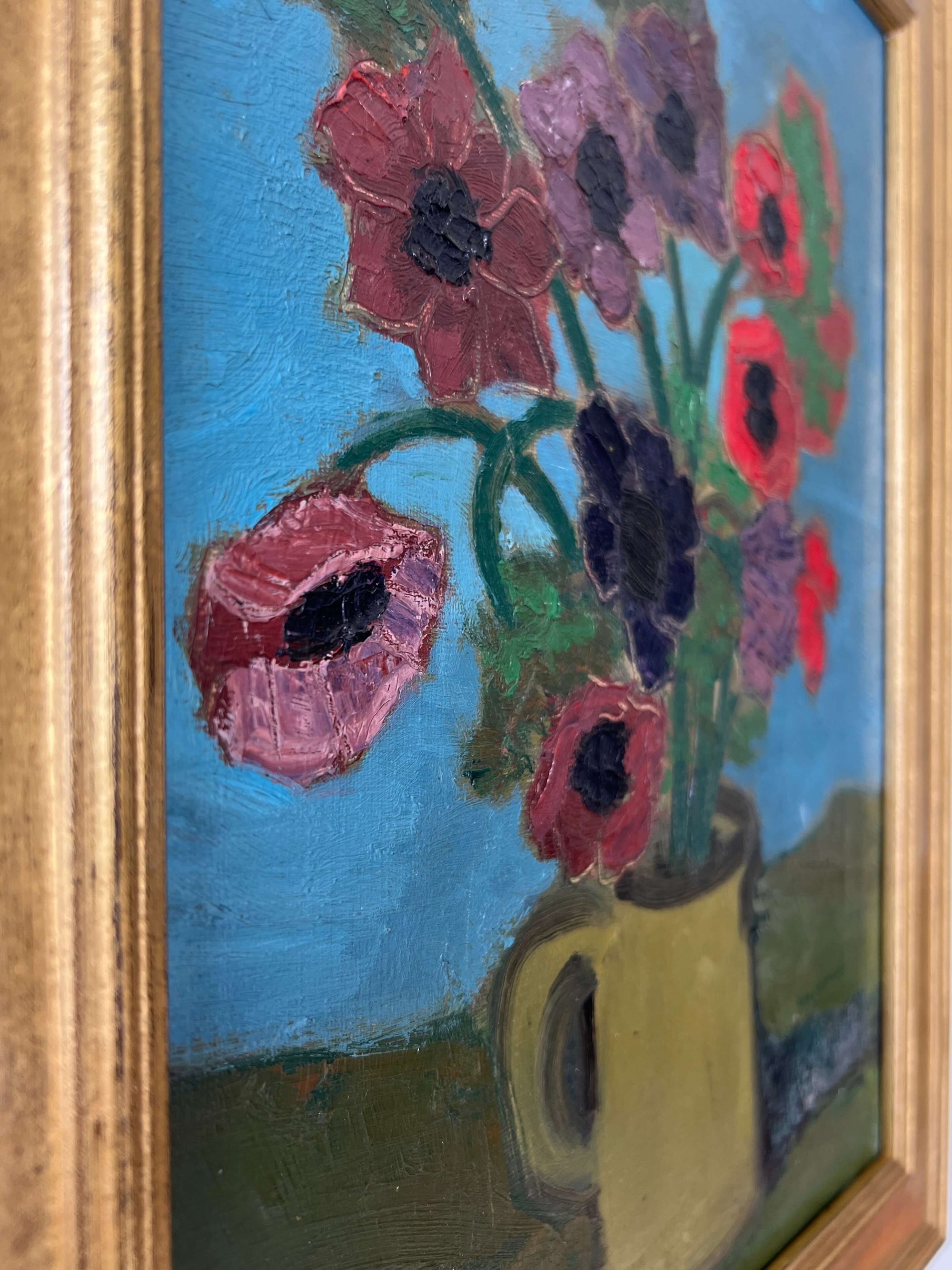 Close up of a framed, vintage artwork of red flowers on a teal blue background.