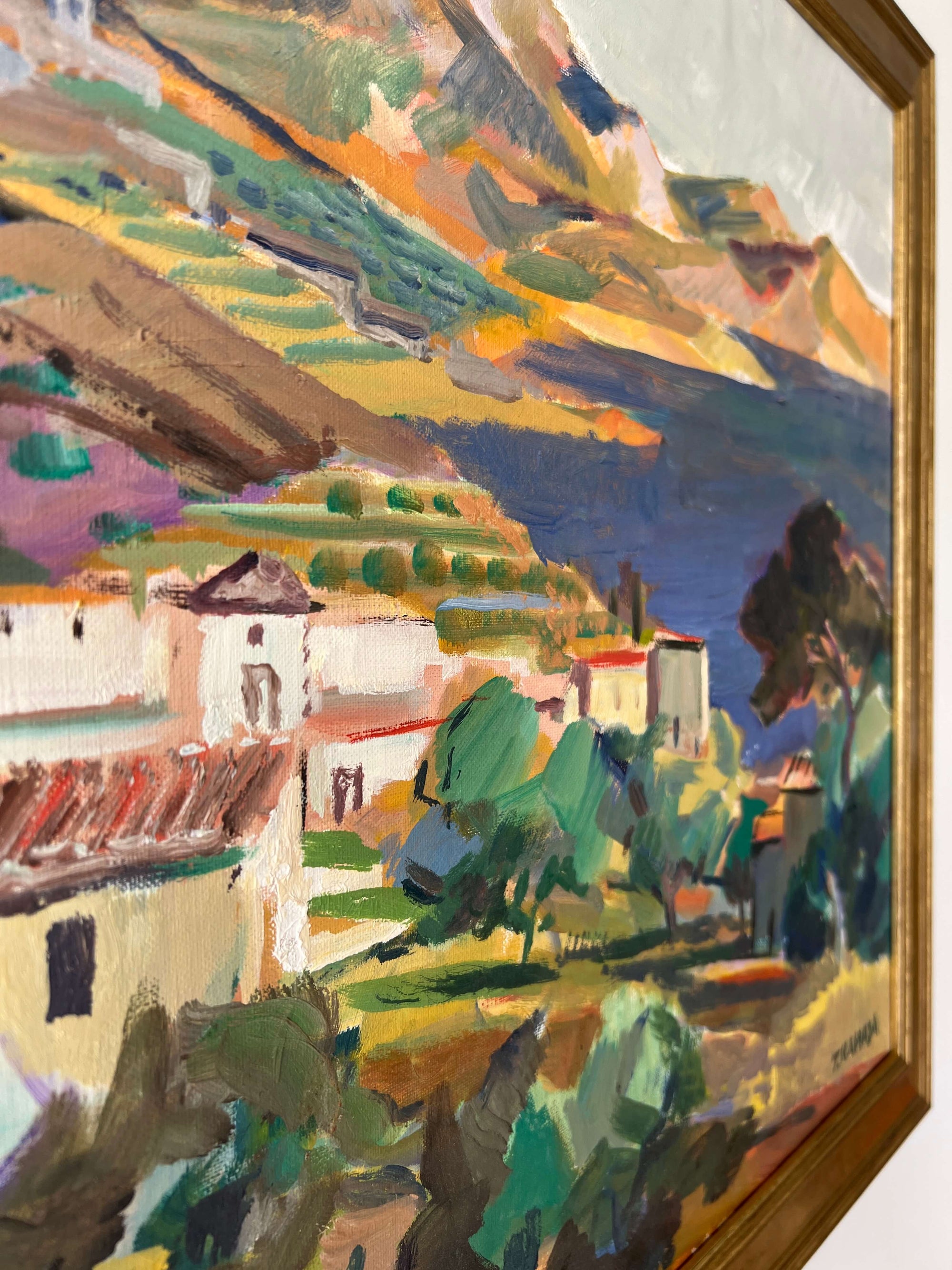 Close up of a framed, vintage oil painting on canvas of a mountainous coastal landscape with houses. Impressionist style.