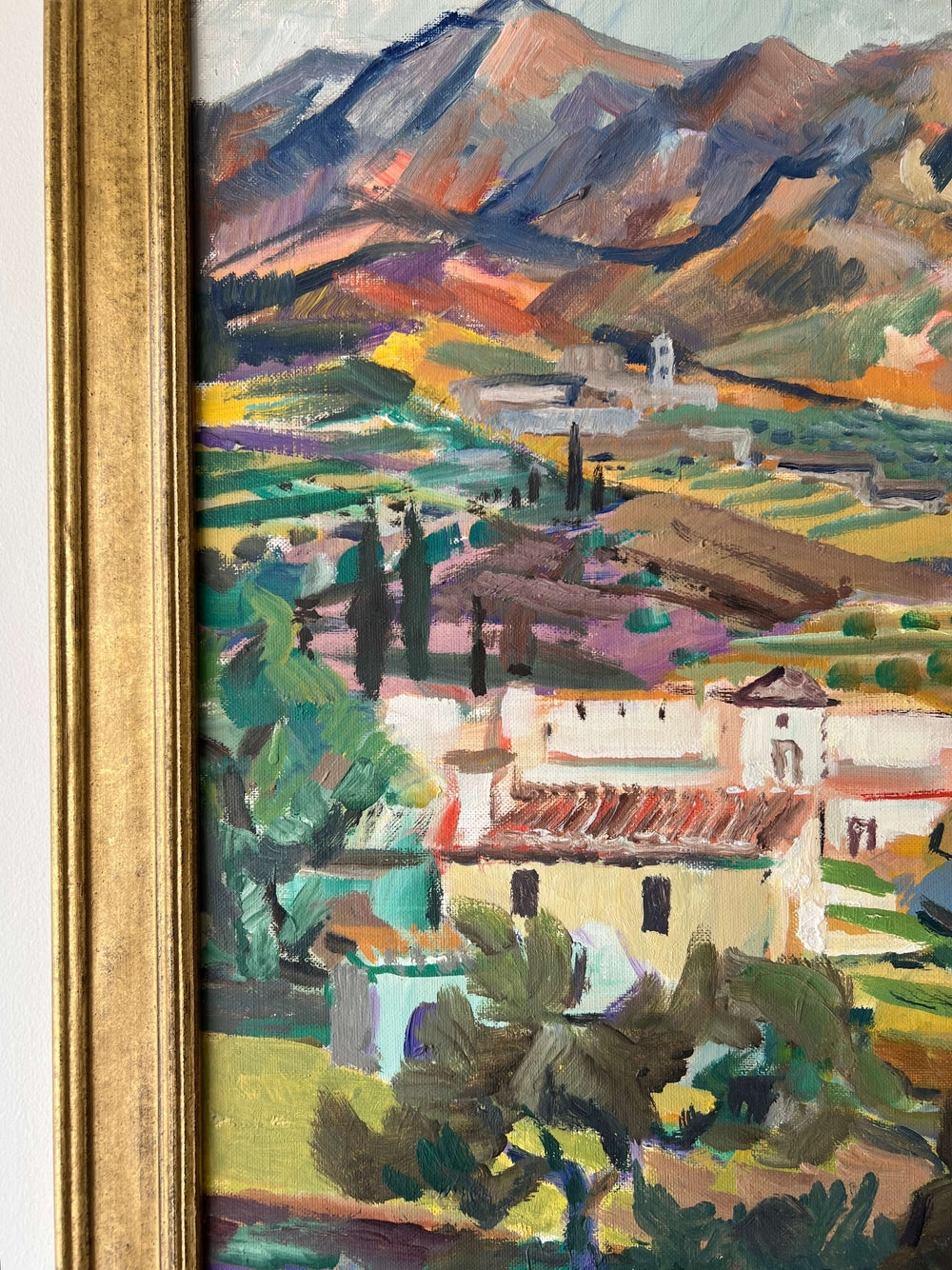Close up of a framed, vintage oil painting on canvas of a mountainous coastal landscape with houses. Impressionist style.