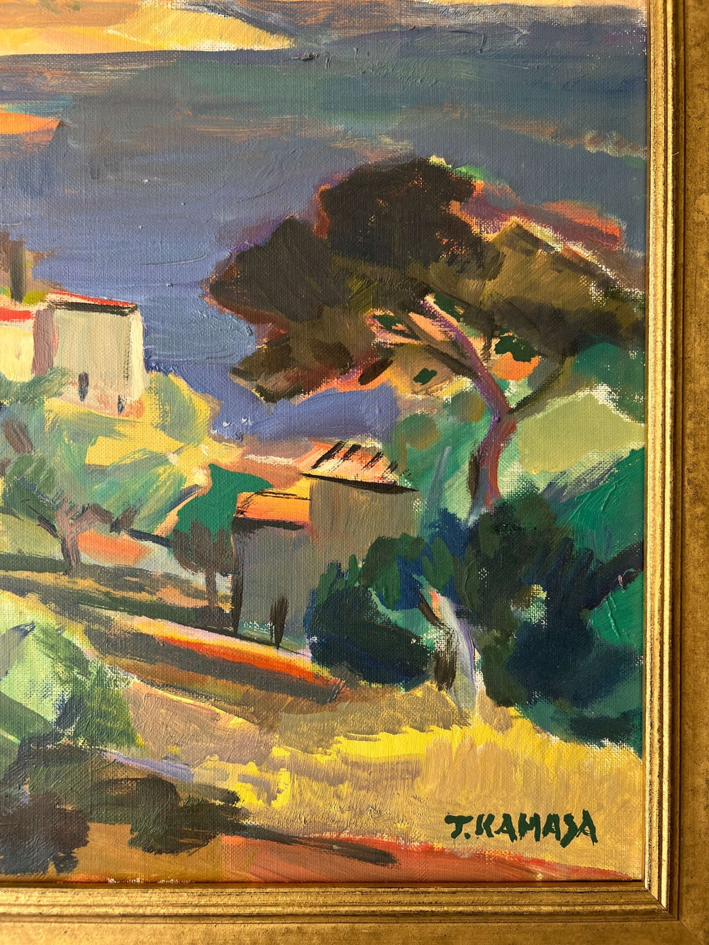 Close up of a framed, vintage oil painting on canvas of a mountainous coastal landscape with houses. Impressionist style.