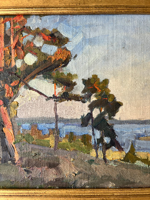 Close up of a framed, vintage oil painting of a landscape with trees and a body of water.
