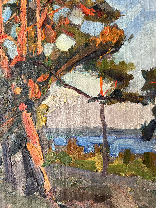 Close up of a framed, vintage oil painting of a landscape with trees and a body of water.