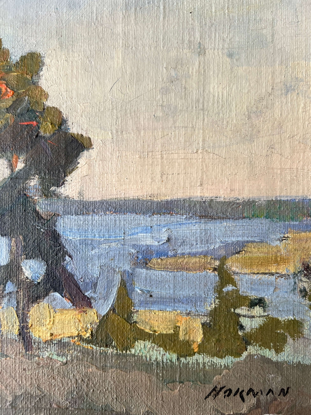 Close up of a framed, vintage oil painting of a landscape with trees and a body of water.