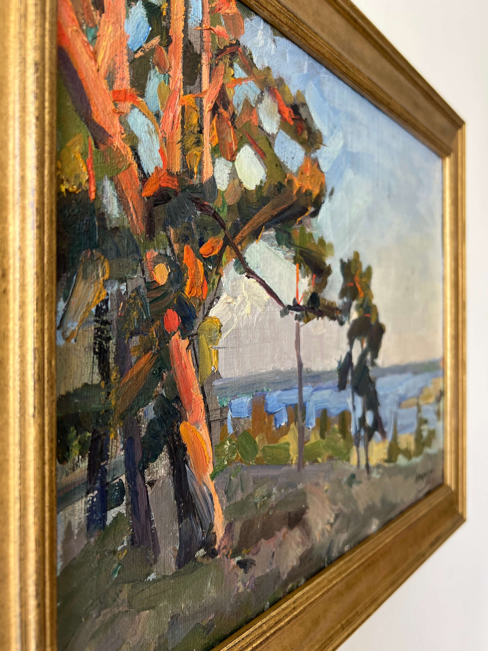 Close up of a framed, vintage oil painting of a landscape with trees and a body of water.