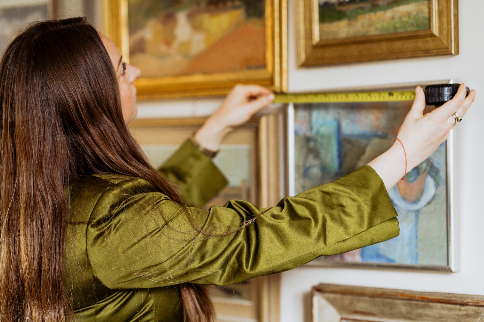 Woman measuring vintage artwork on a wall with a tape measure