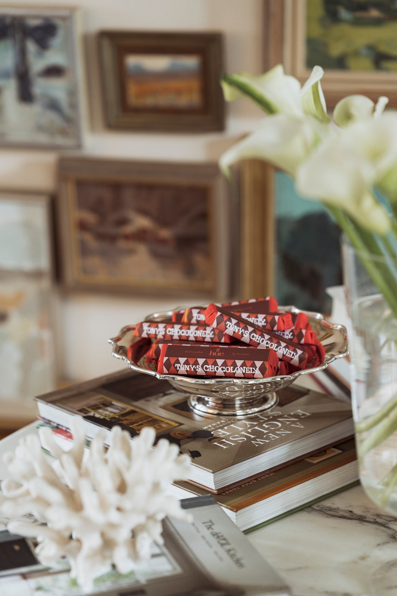 Branded chocolate bars in a silver dish on top of books with a vase of white flowers in the background.