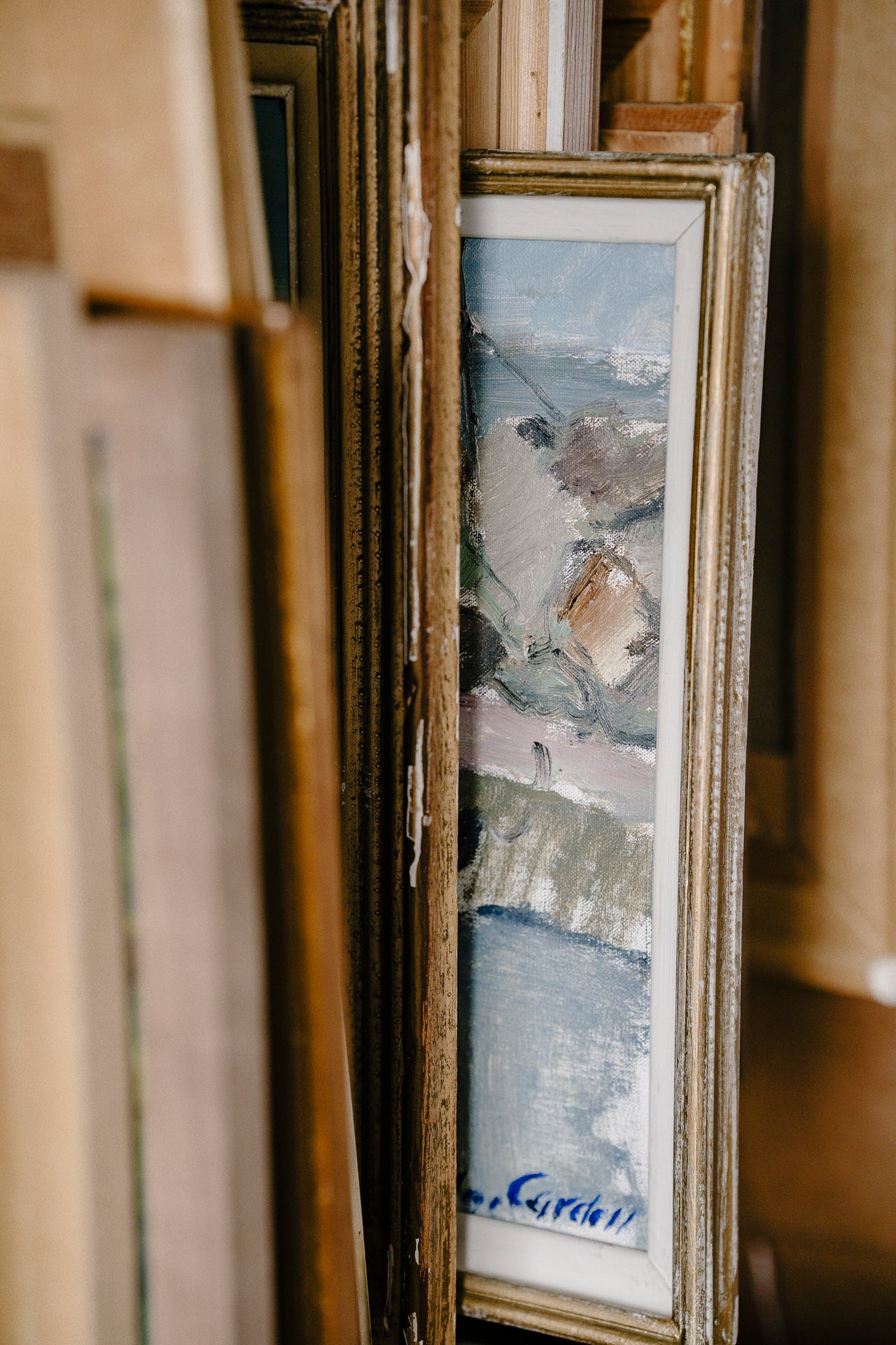 Vintage painting inside an ornate frame poking out from a rack of paintings
