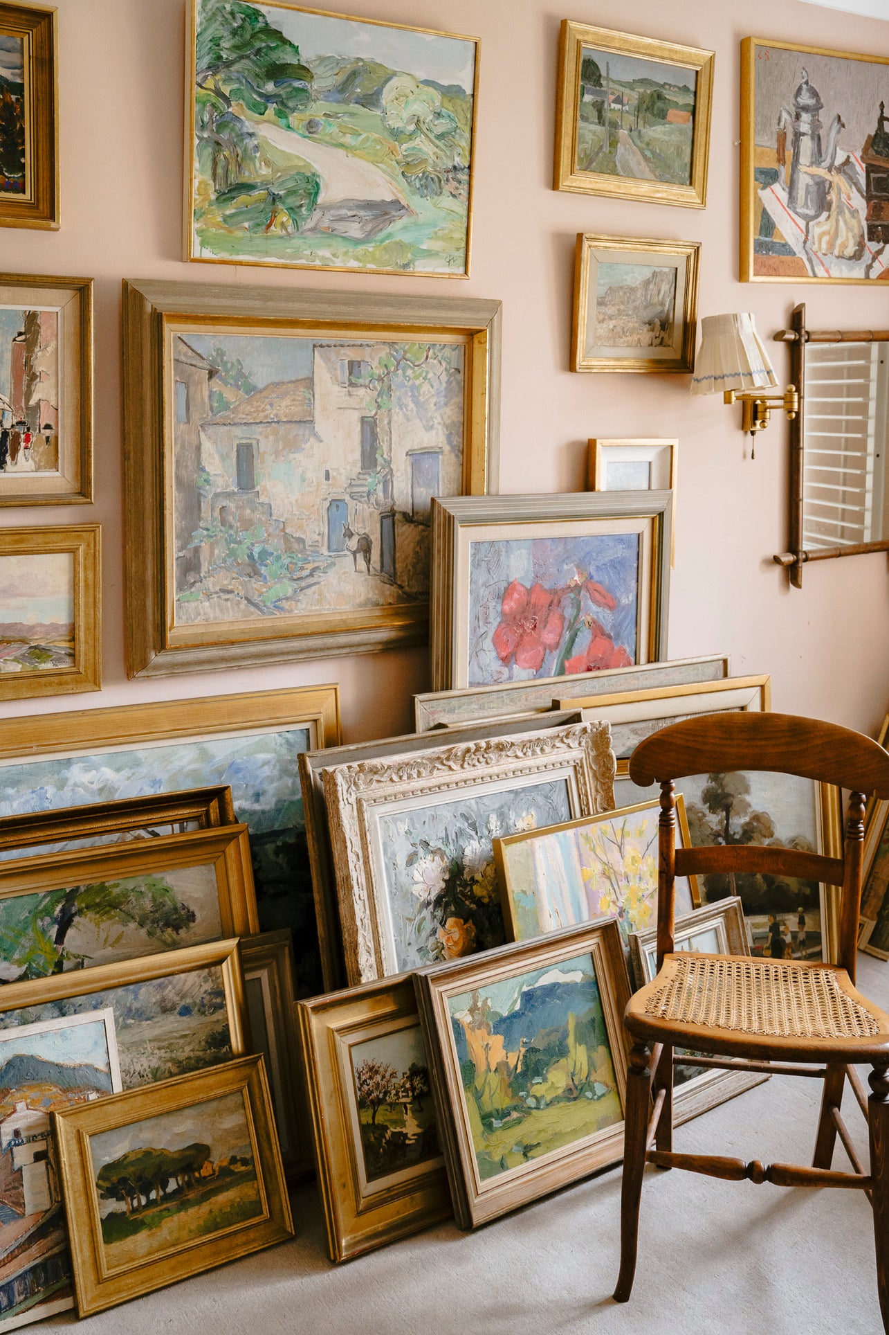Wall with various framed vintage paintings and a chair in a room.