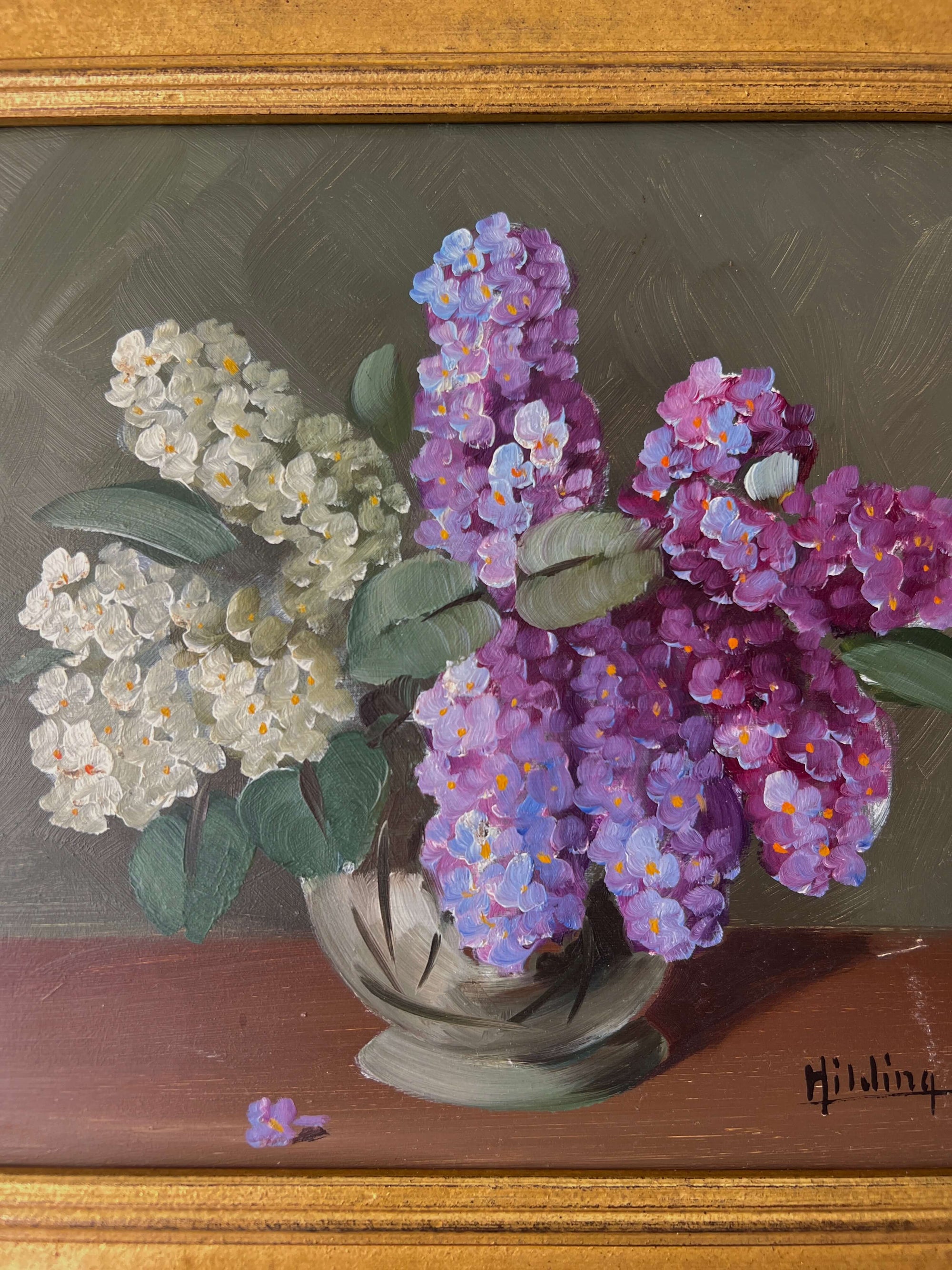 Close up of a framed, vintage artwork of purple and white flowers on a dark background.