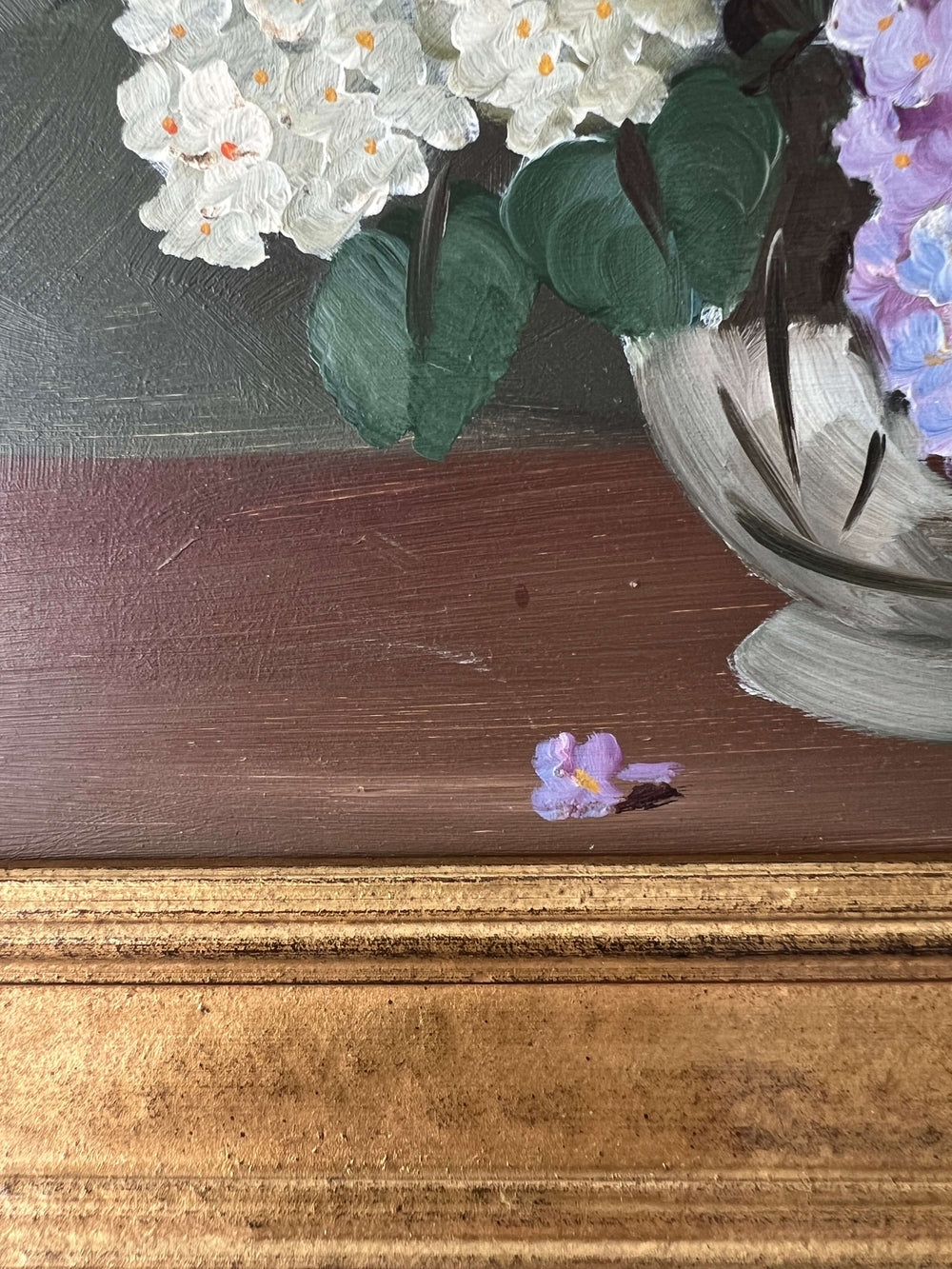 Close up of a framed, vintage artwork of purple and white flowers on a dark background.