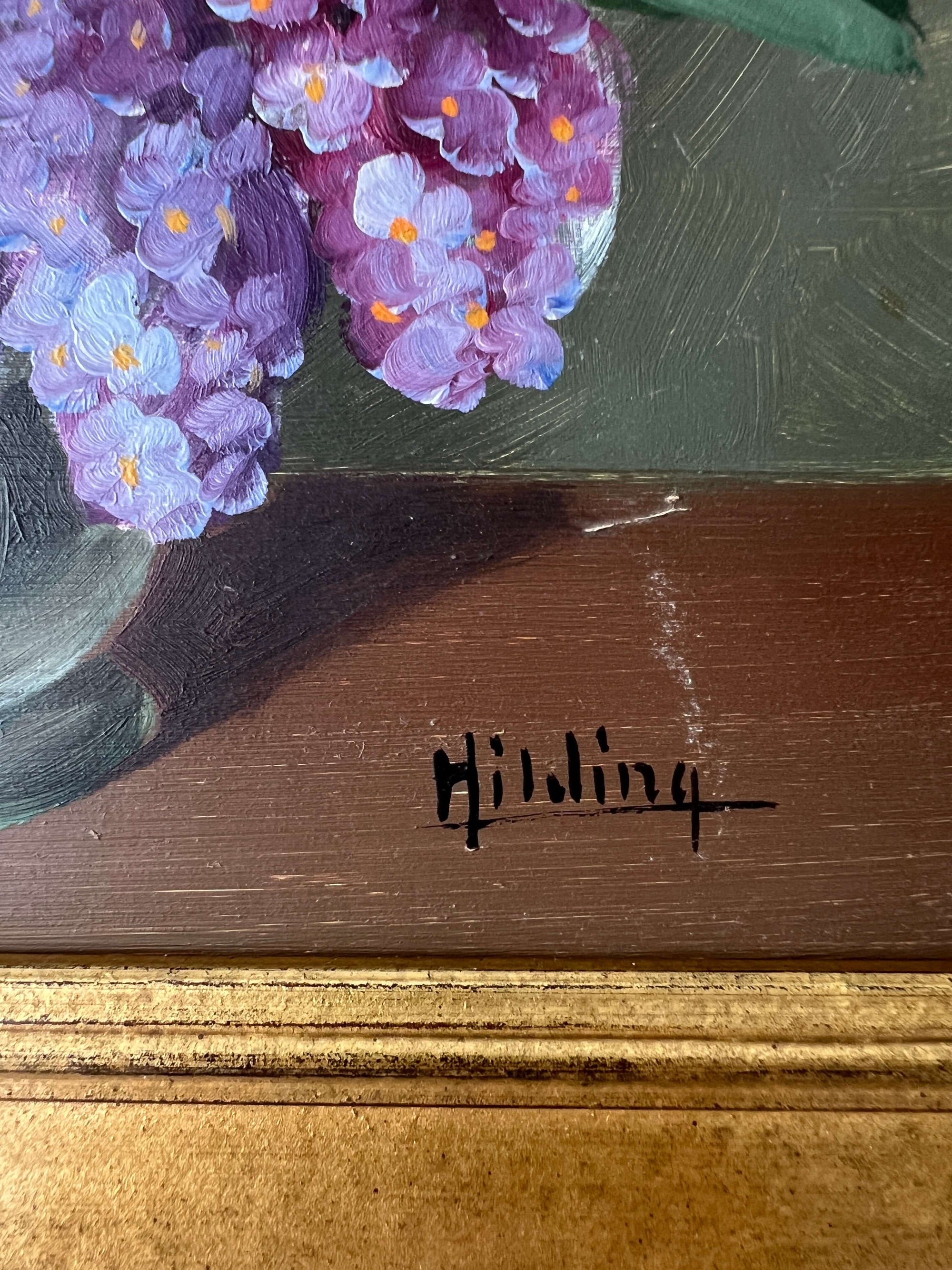 Close up of a framed, vintage artwork of purple and white flowers on a dark background.