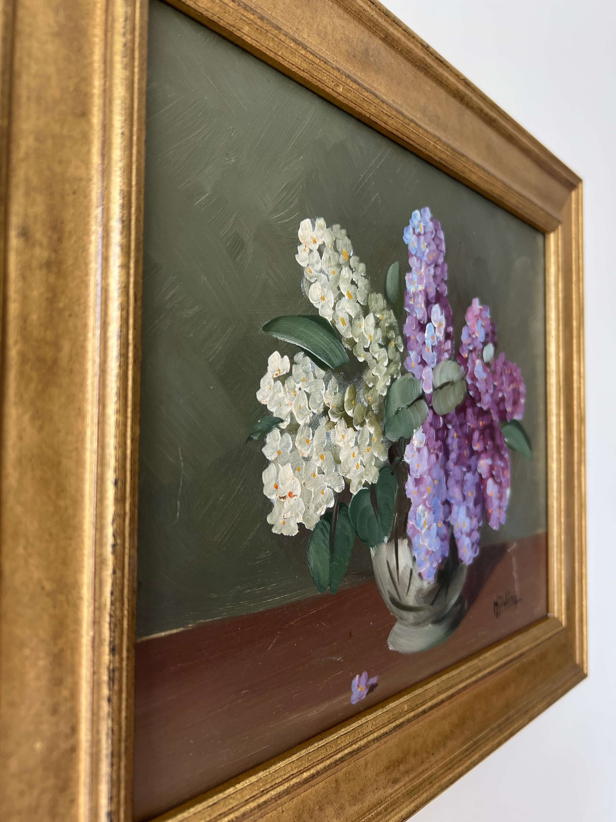 Close up of a framed, vintage artwork of purple and white flowers on a dark background.