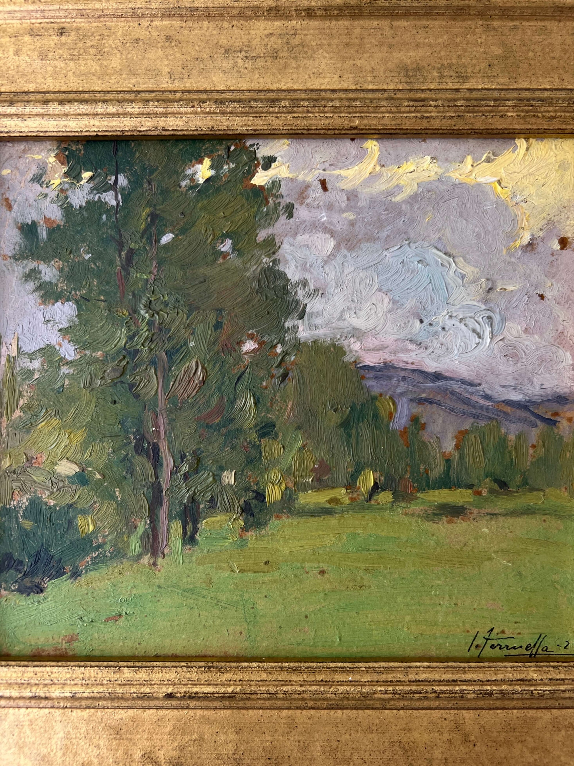 Close up of a framed vintage oil painting of a landscape with trees and a meadow.