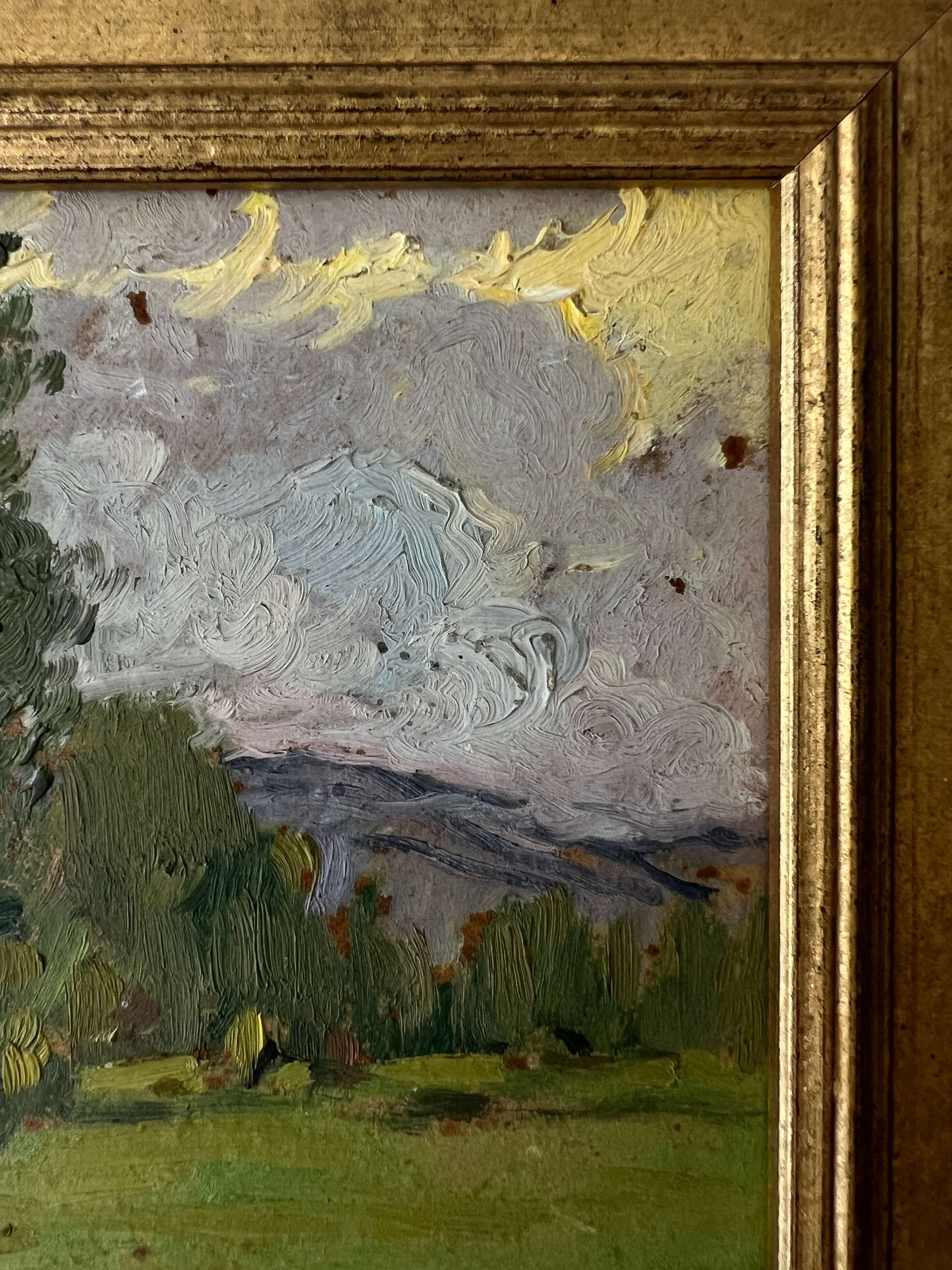 Close up of a framed vintage oil painting of a landscape with trees and a meadow.