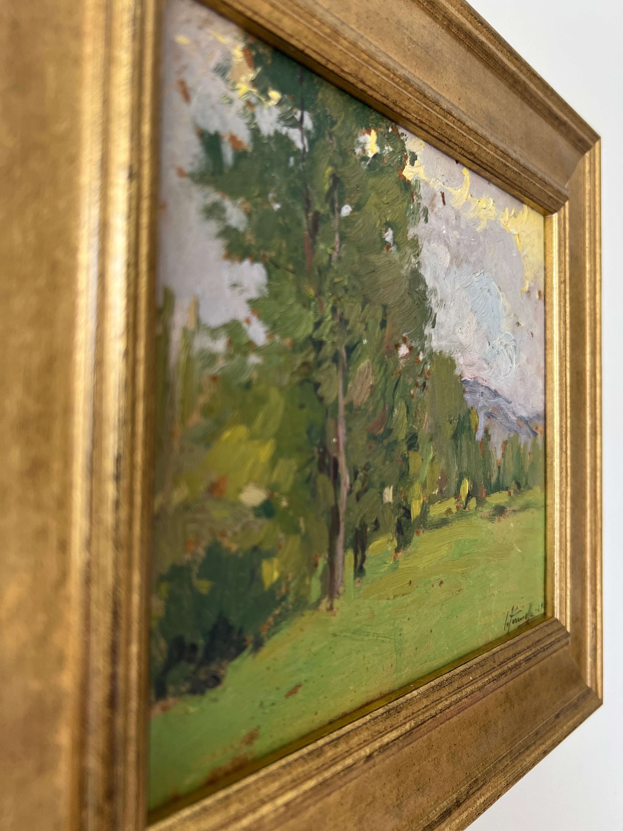 Close up of a framed vintage oil painting of a landscape with trees and a meadow.