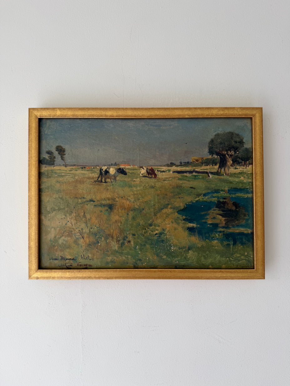 A framed vintage landscape oil painting depicting a grassy field with cows, a tree, and a small pond, housed in a gold-toned frame. Available at Hue. 