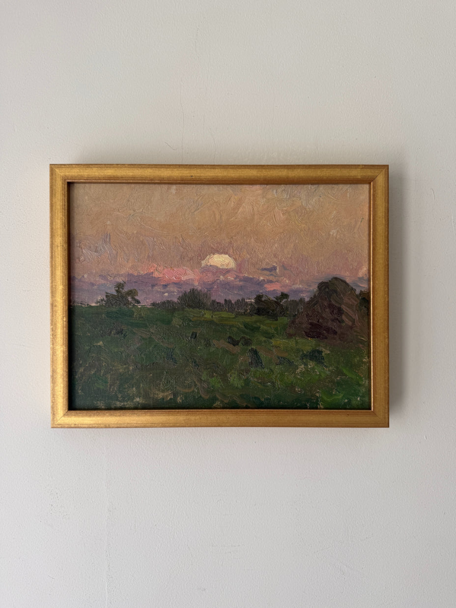 A framed vintage landscape oil painting from the mid-century. The painting depicts a green field under a warm, sunset-coloured sky with a glowing sun and distant hills, enclosed in a gold frame. Available at Hue.