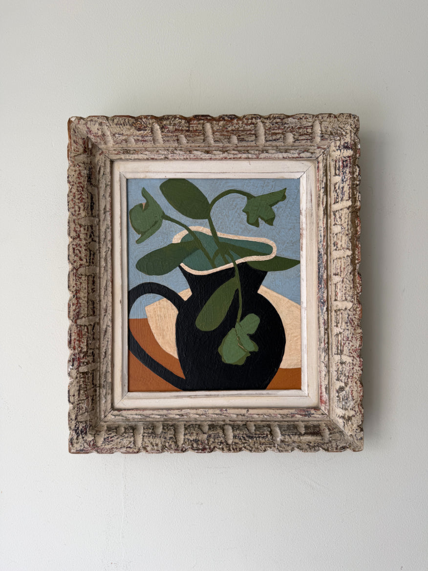 A framed still life painting featuring a black pitcher with green leaves on a light blue and brown background, housed in a distressed, ornate textured frame. Available at Hue. 
