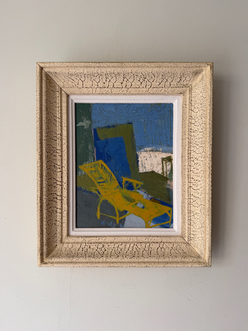 A framed abstract painting featuring a bright yellow lounge chair against a blue and green background, housed in a textured cream-colored frame. Available at Hue. 