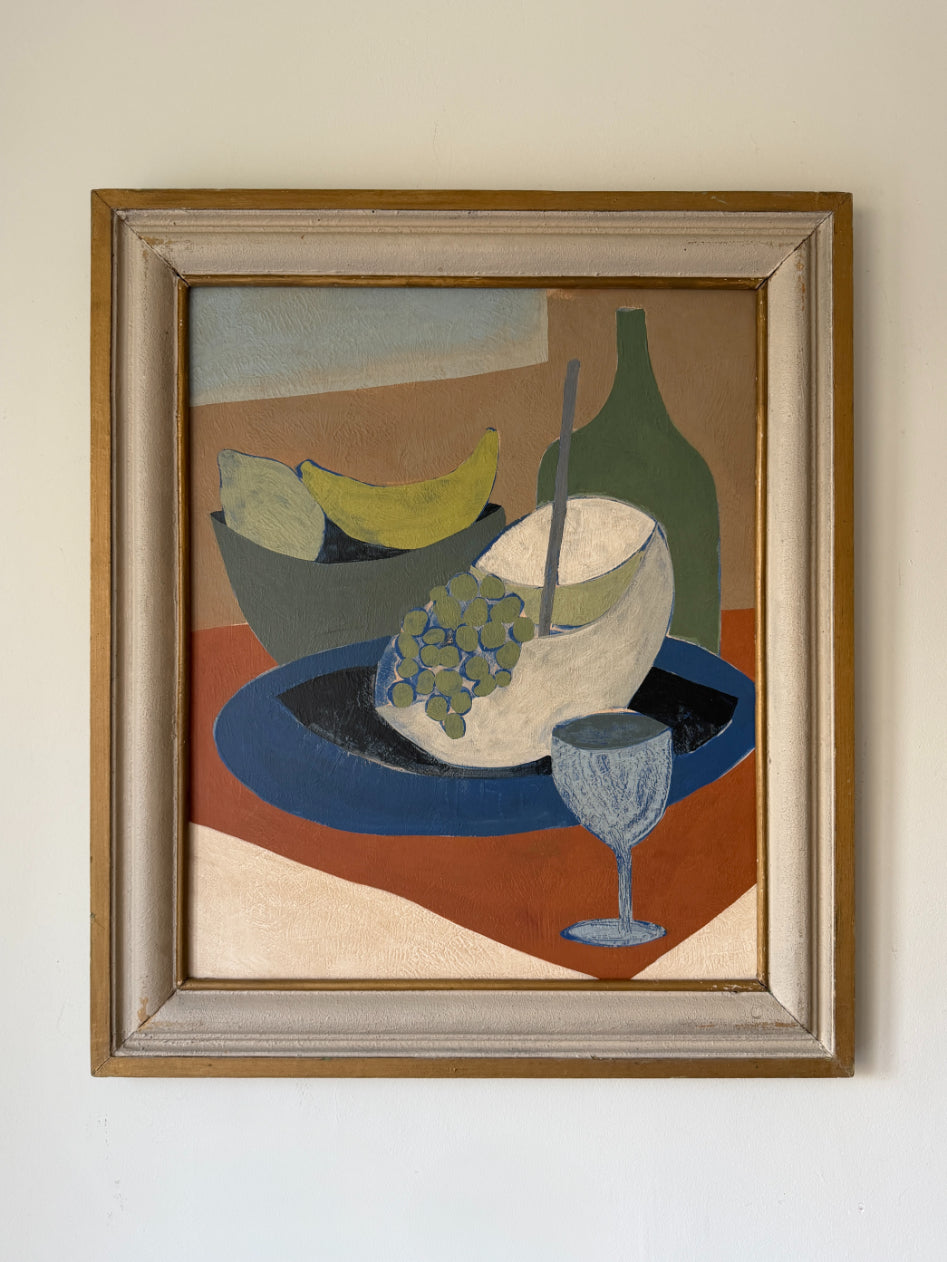 A framed still life painting. The artwork features a stylized arrangement with a blue plate, a white fruit, green grapes, a green bottle, and a blue glass, enclosed in a light wood frame. Available at Hue. 