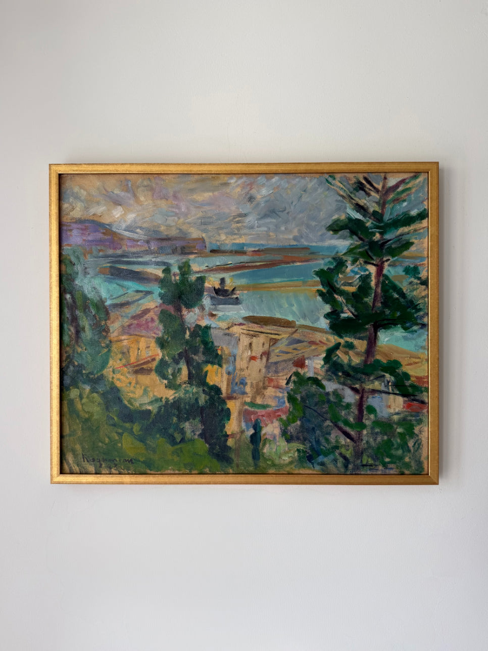 A framed vintage landscape painting depicting a coastal village with trees, water, and buildings rendered in textured brushstrokes of green, blue, yellow, and purple tones, enclosed in a gold frame. Available at Hue. 