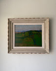 A framed vintage landscape painting of green fields and distant hills under a blue sky, housed in a distressed, light-colored wooden frame. Available at Hue.