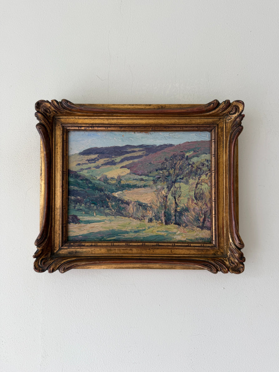 Framed vintage oil painting of a rolling green landscape in France. Presented in an ornate gilt frame. Available at Hue. 